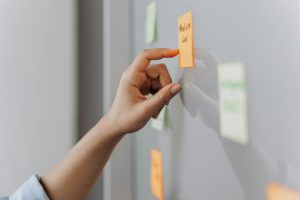 A hand placing a sticky note on a reflective surface in an office setting.